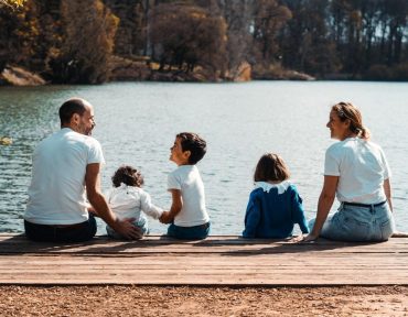 A family of five relaxing by a serene lake in Lyon, France on a sunny day.